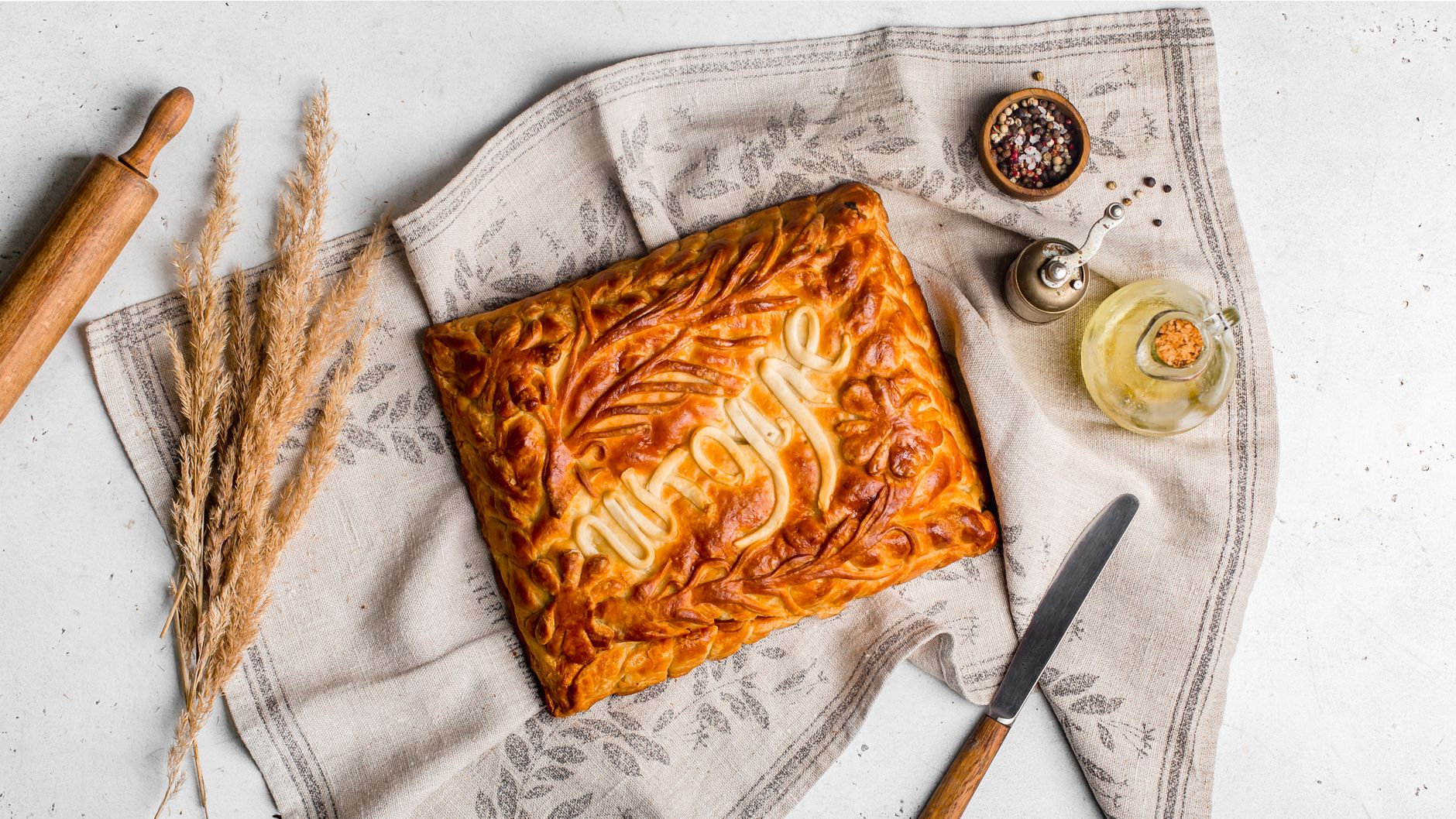 Artistic presentation of a rustic pie with spices and kitchen tools on a linen cloth.