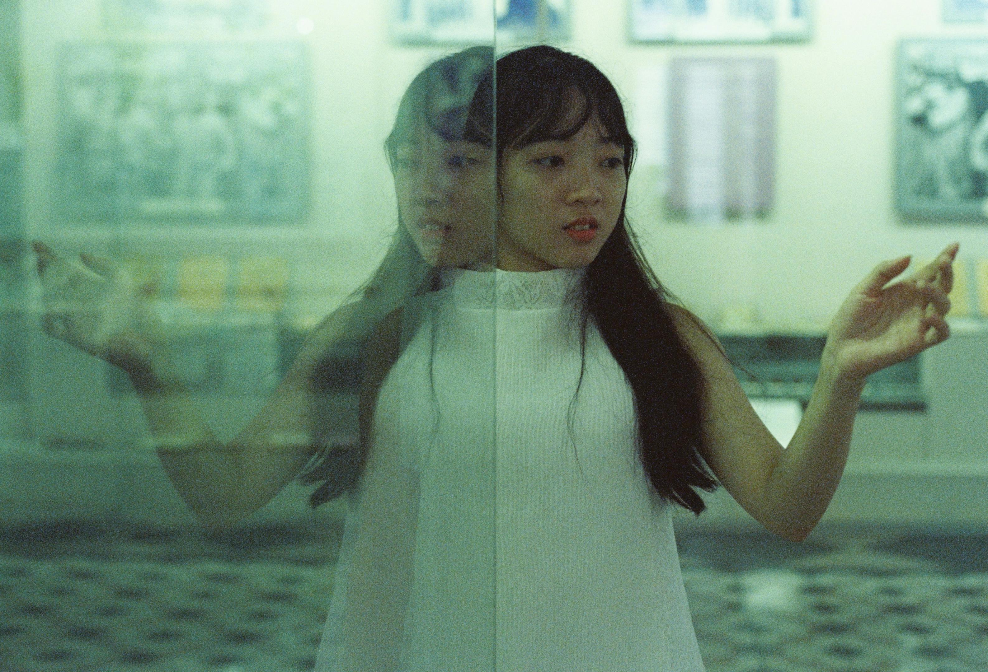 A woman gazes at her reflection in a glass surface, creating an artistic and introspective moment.