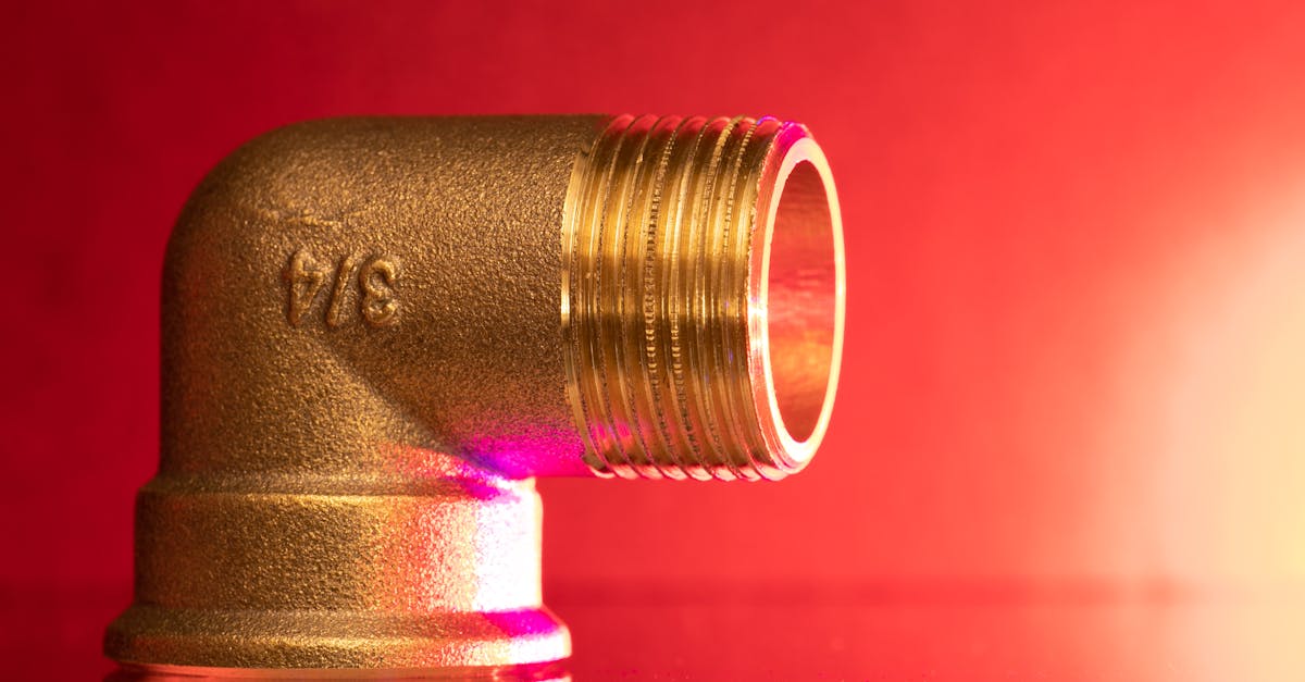 Close-up of a shiny brass pipe elbow fitting against a vibrant red backdrop, showcasing industrial elegance.