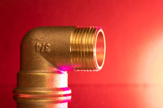 Brass pipe elbow fitting on red backdrop.