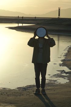 Silhouette of a person with a reflector by a tranquil coastal area during sunset.
