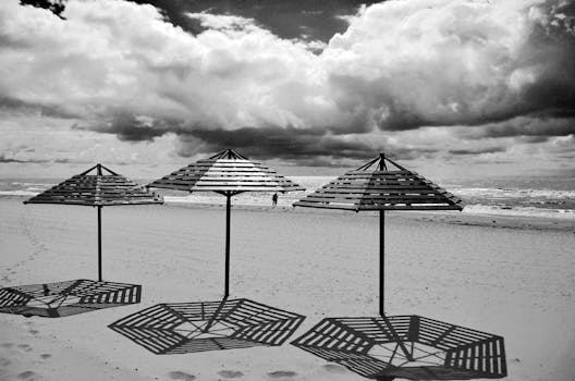 Dramatic black and white image of a beach with umbrellas and cloudy sky.