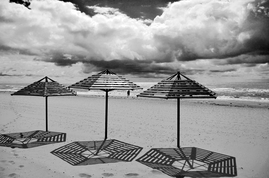 Dramatic black and white image of a beach with umbrellas and cloudy sky.