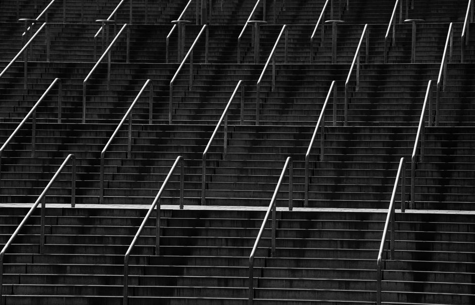 Symmetrical black and white photo of stairs with metal handrails creates an abstract pattern.
