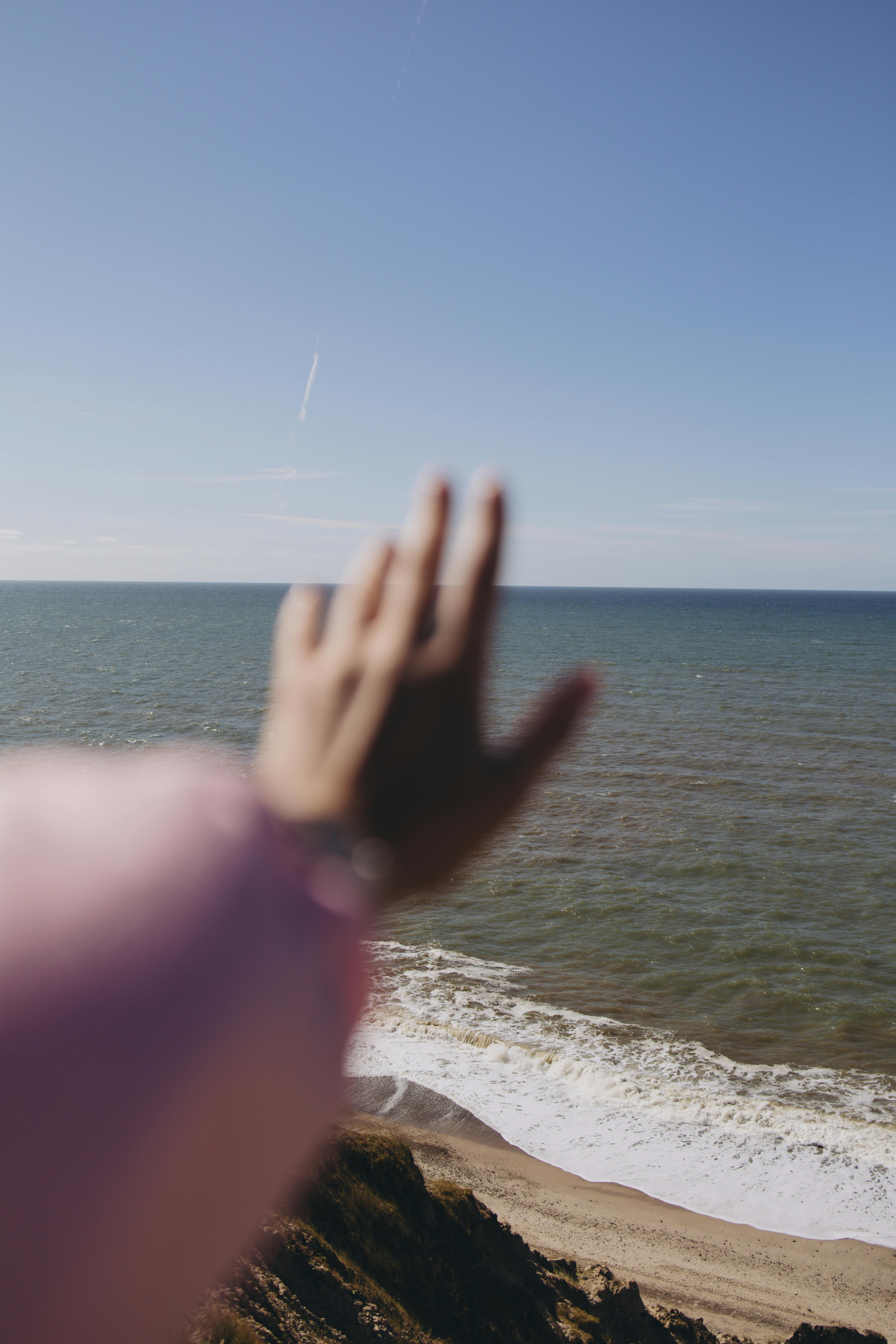 A person reaches toward the ocean, capturing a serene moment of connection with nature.