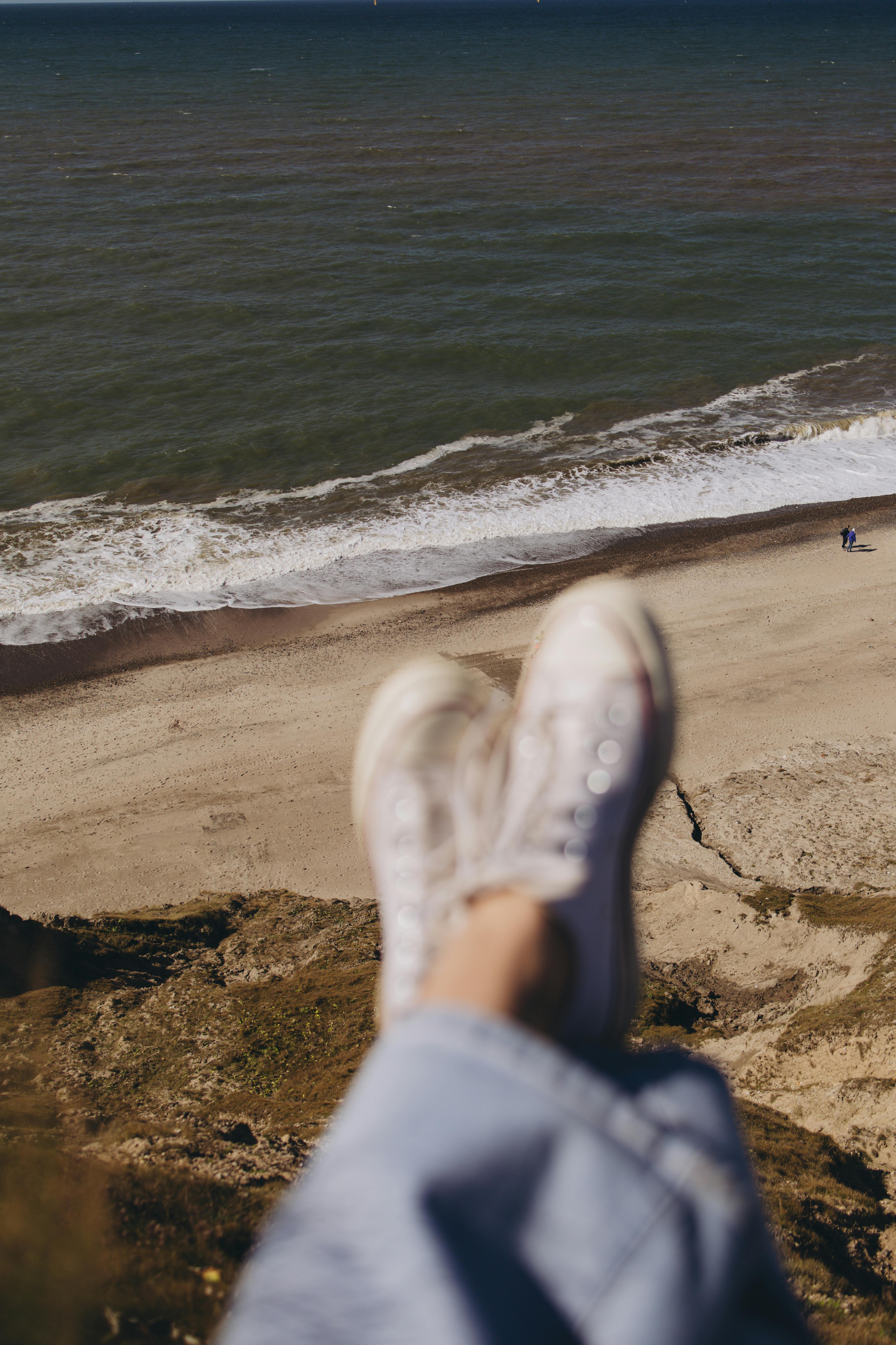 A serene beach view from a cliff with sneakers in the foreground, evoking a sense of relaxation.