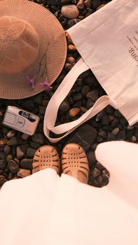 Top view of summer beach accessories including hat, bag, and sandals on a pebble surface.