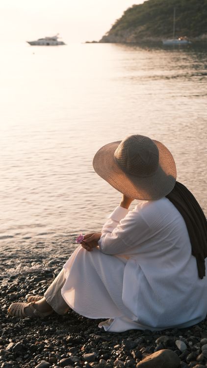 A woman in a white hat sits on the beach · Free Stock Photo