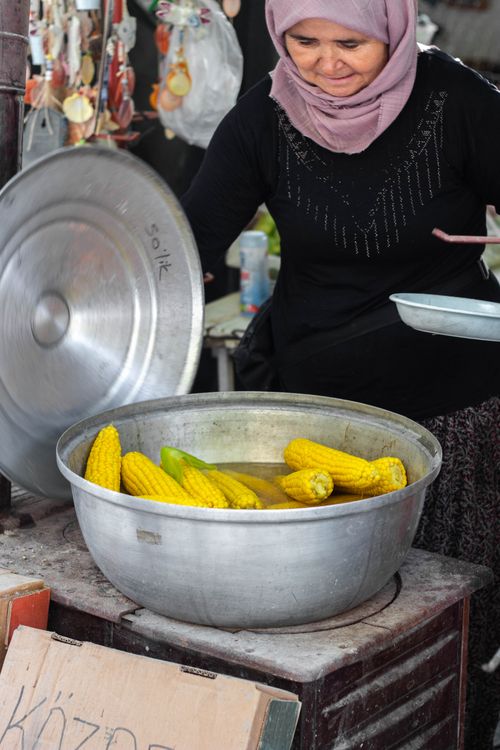 Free A woman wearing a hijab cooks corn in a large pot at a bustling local market. Stock Photo