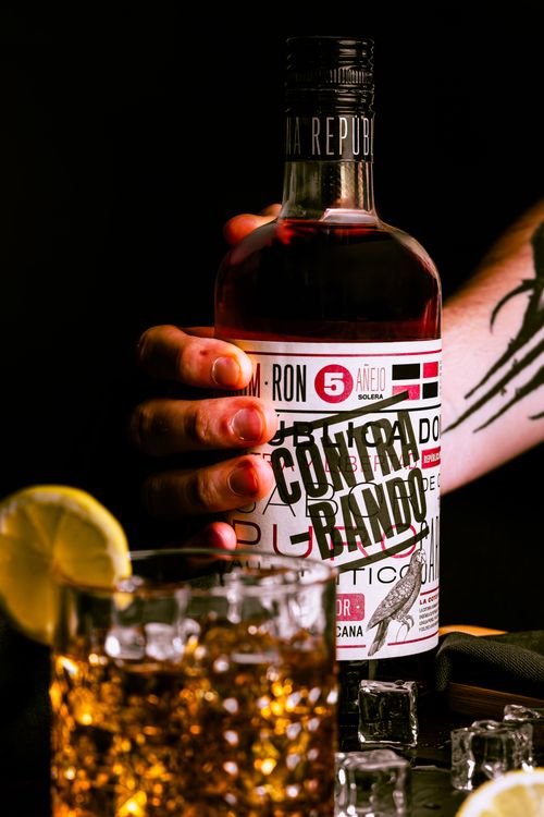 Free Close-up of tattooed hand with rum bottle and cocktail, ideal for nightlife themes. Stock Photo