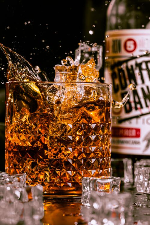Free A dynamic shot of whiskey splashing in a crystal glass with ice cubes, exuding luxury and refreshment. Stock Photo