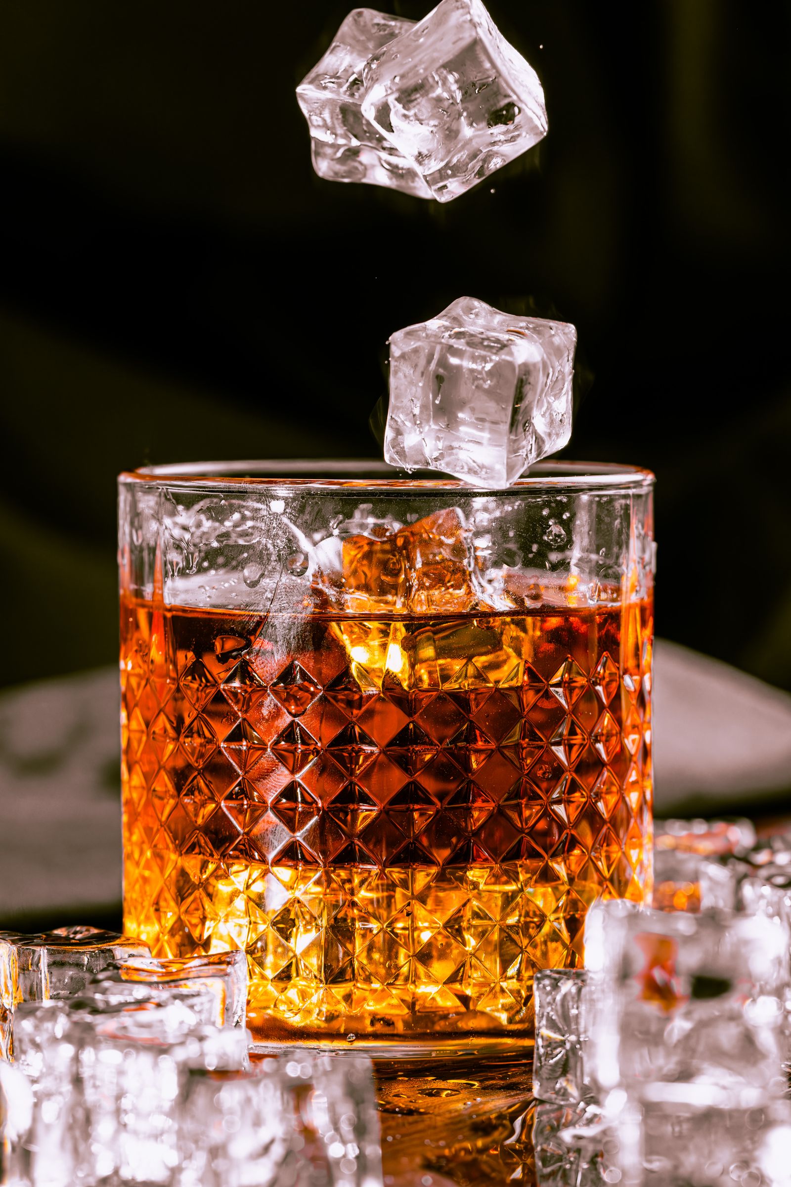Vaso de whisky iluminado dramáticamente con cubos de hielo cayendo