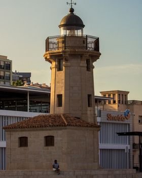 Sunset view of the El Grao de Castellón lighthouse with a person nearby, showcasing local architecture.