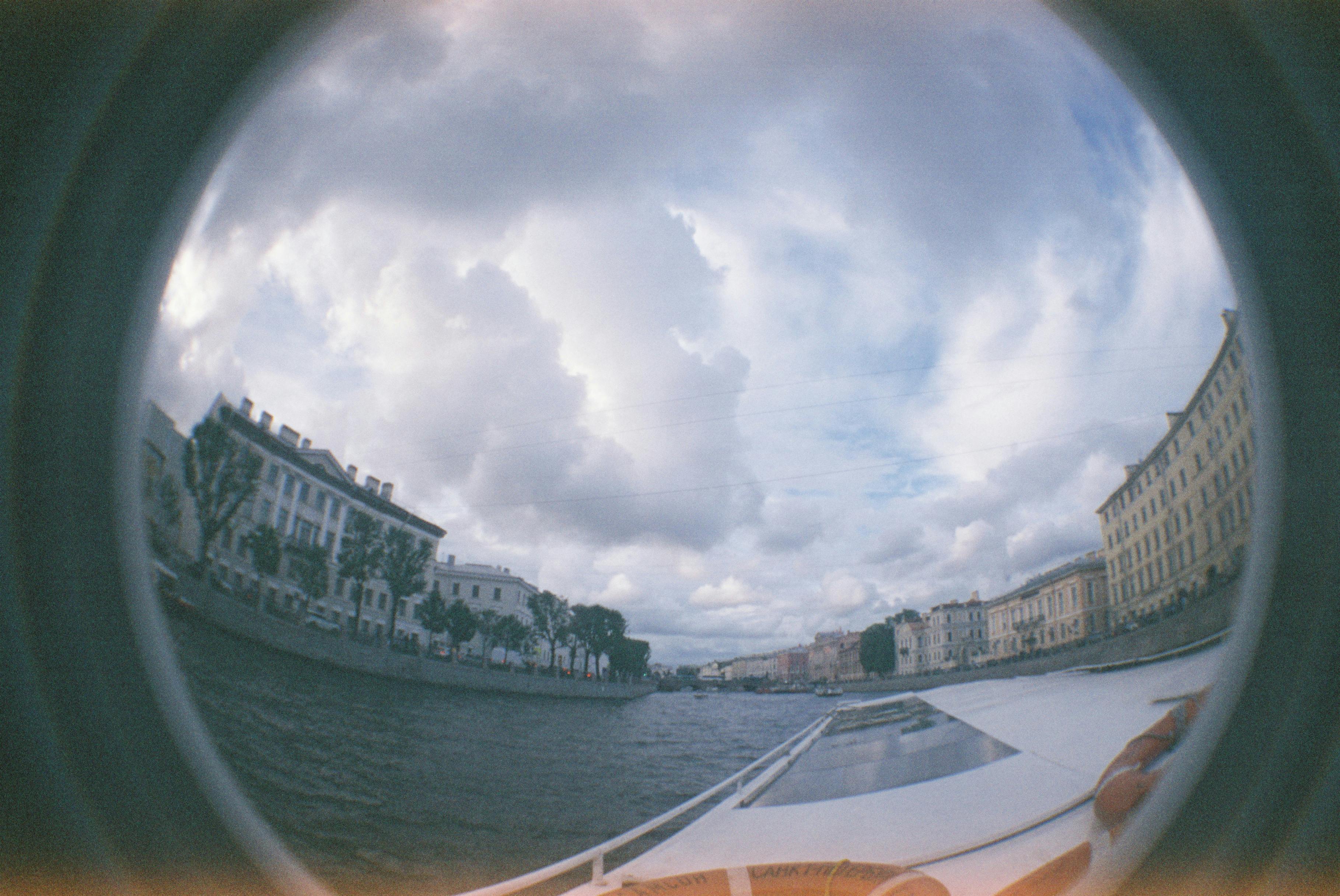Fisheye lens captures cityscape and river under a dramatic cloudy sky.