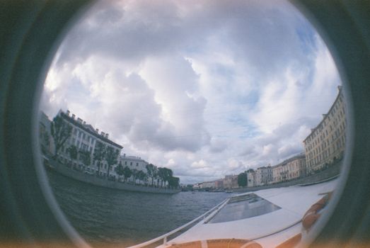 Fisheye lens captures cityscape and river under a dramatic cloudy sky.