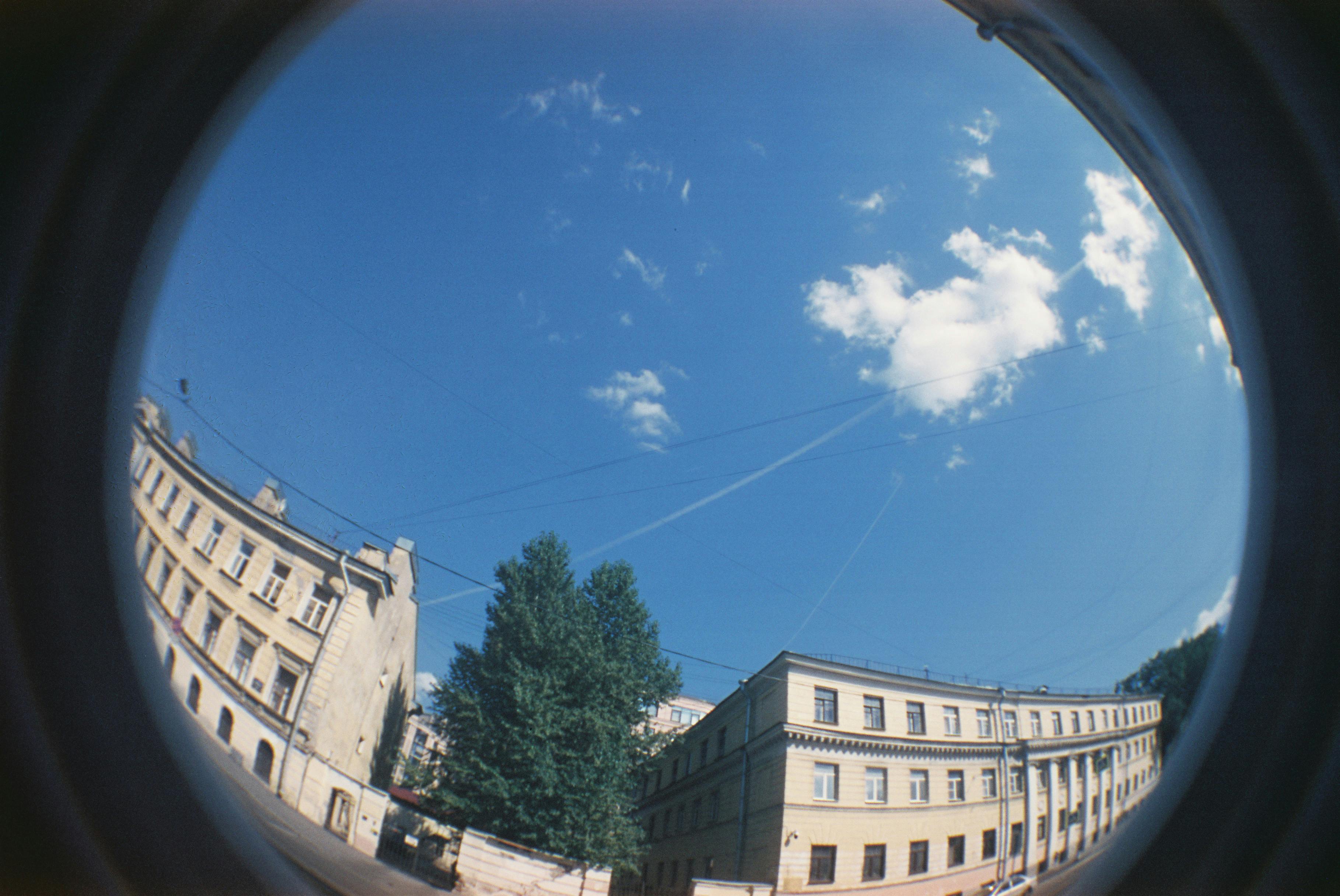 Cityscape through fisheye lens with historical buildings and blue sky.