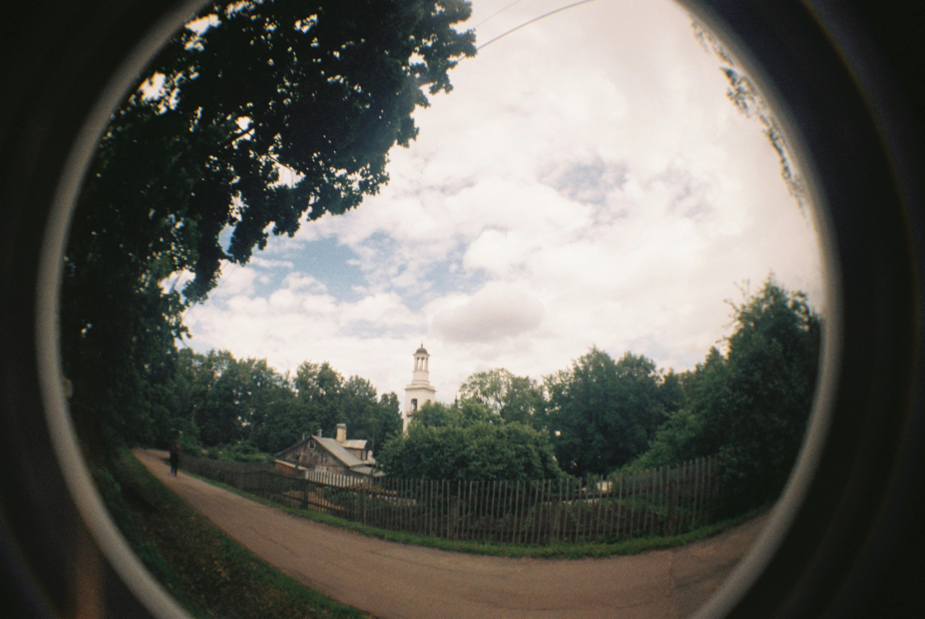 Fisheye lens captures a tranquil rural scene with a church spire and lush greenery.