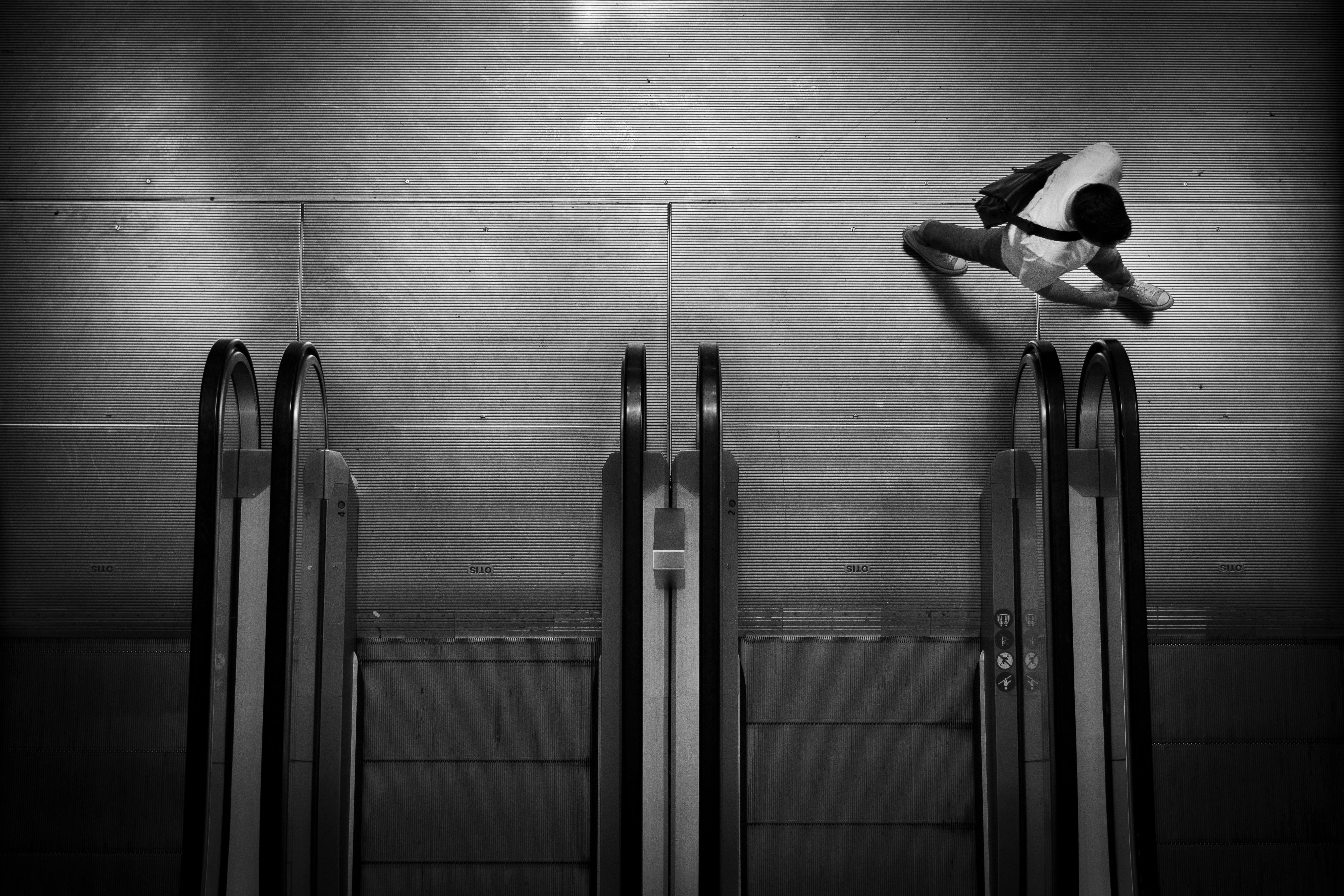 Black and white photo of a man walking by escalators in an urban setting. Moody and sleek.