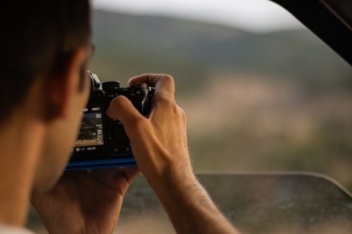 Free An adult male taking a photograph with a digital camera, focusing on an outdoor landscape. Stock Photo