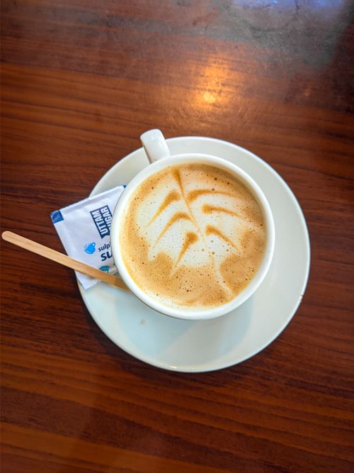 Free A cappuccino with elegant froth art served on a wooden table with sugar pack and stirrer. Stock Photo