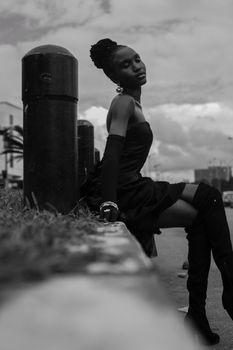 Elegant woman posing in urban setting, black and white photography, wearing fashionable black dress and boots.