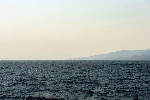 Free Peaceful ocean scene with distant mountain silhouette under a clear sky. Stock Photo