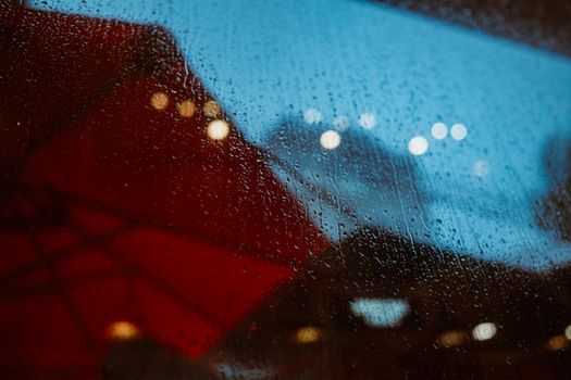 Raindrops on a window with colorful abstract reflections and blurred lights.