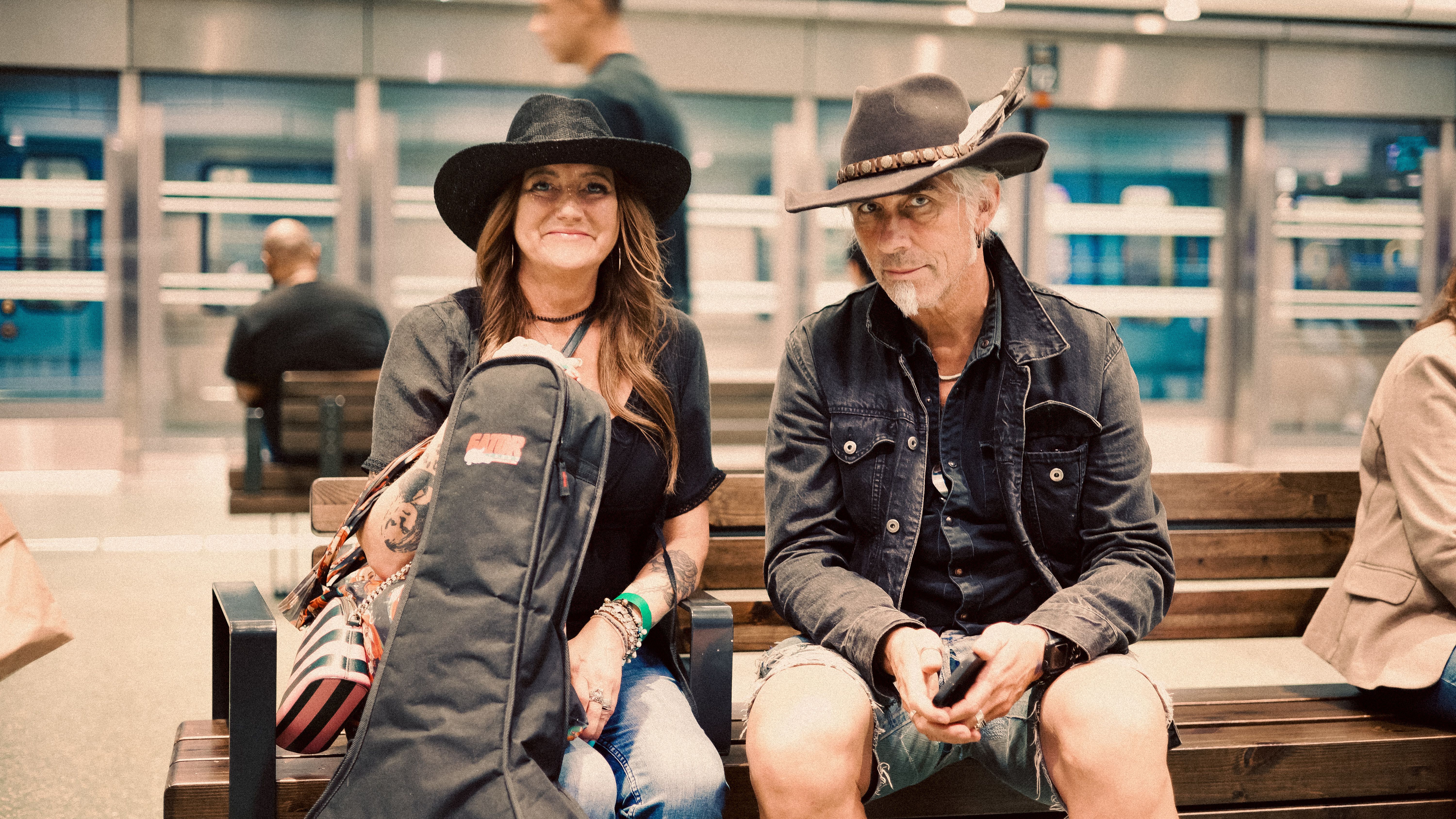 A fashionable couple with hats sitting on a bench at a train station.