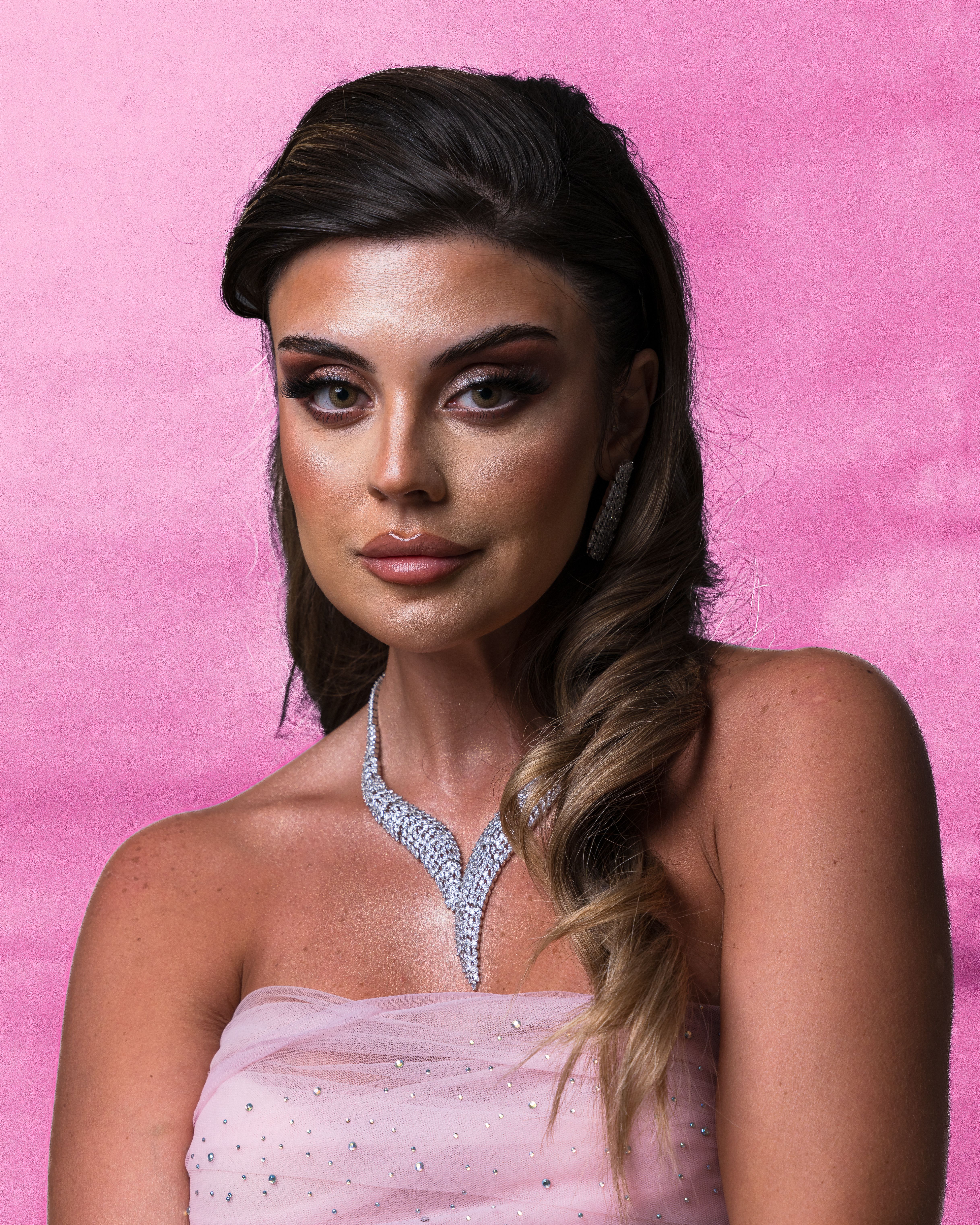 Portrait of an elegant woman in a pink dress with striking makeup against a pink backdrop.