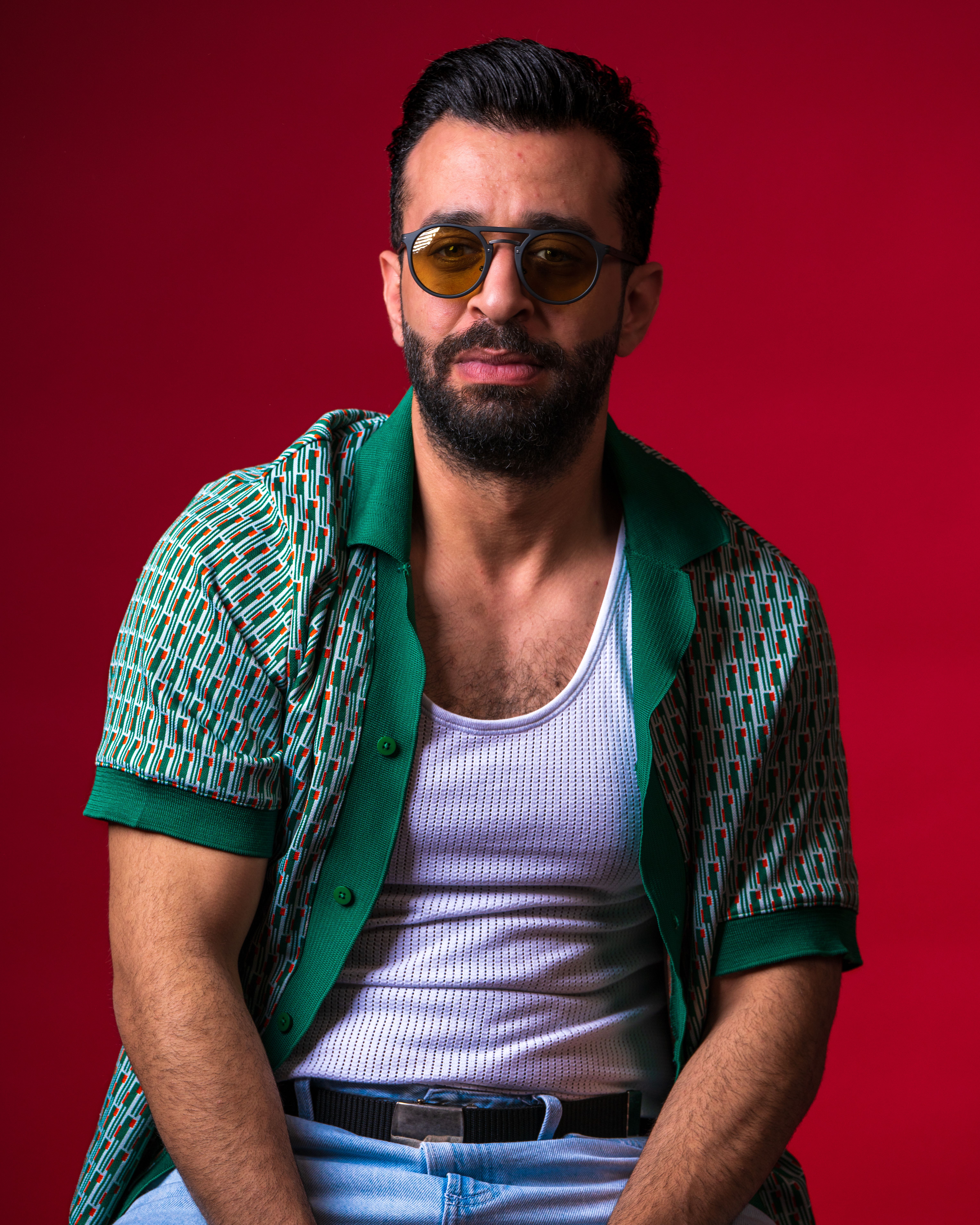 Portrait of a man with beard and sunglasses against a vibrant red background