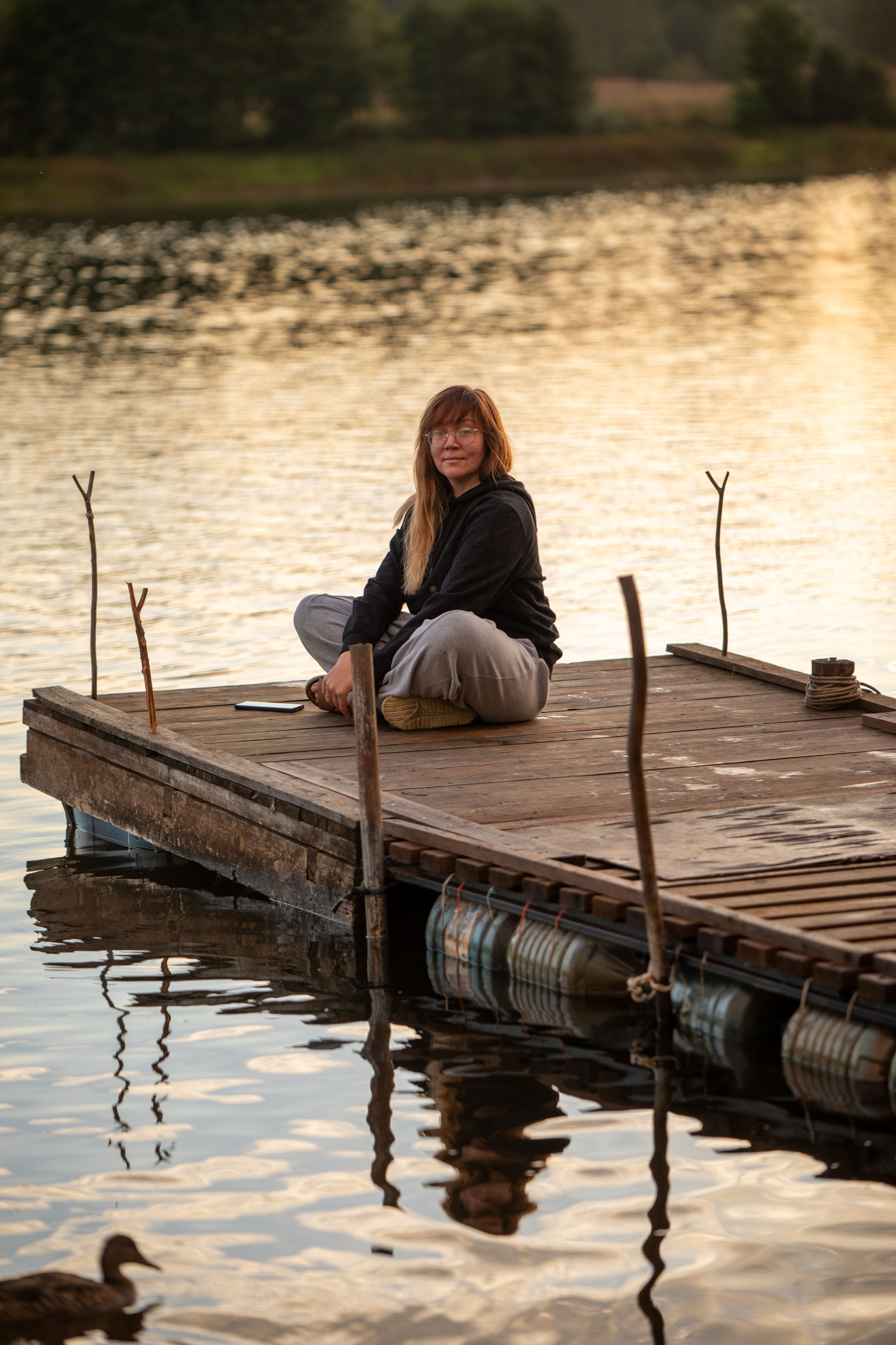 A woman sits peacefully on a wooden pier by the lake during sunset, reflecting tranquility.