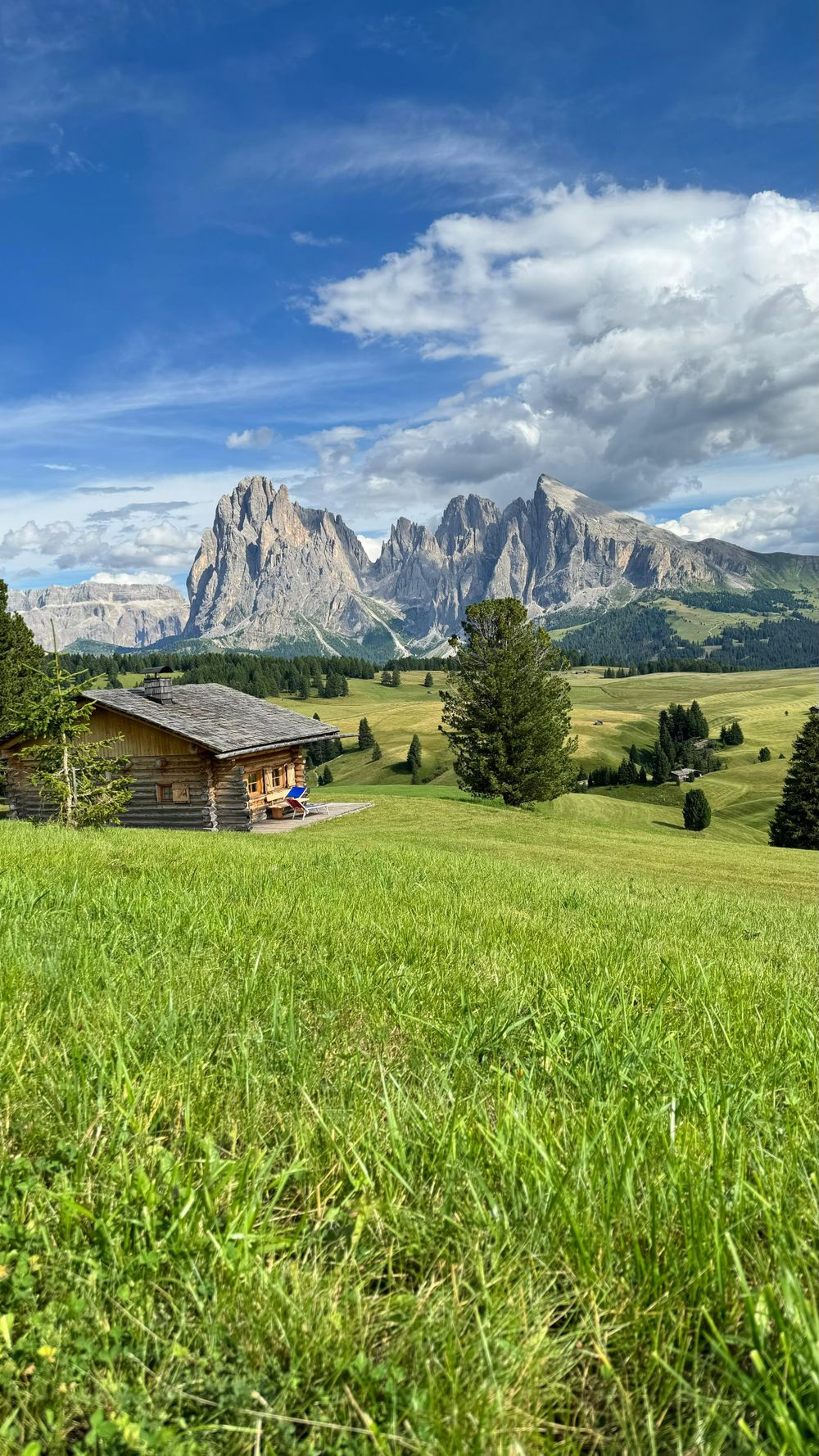 Cabană de lemn pe pajiștile de pe Alpe di Siusi, cu munții în fundal