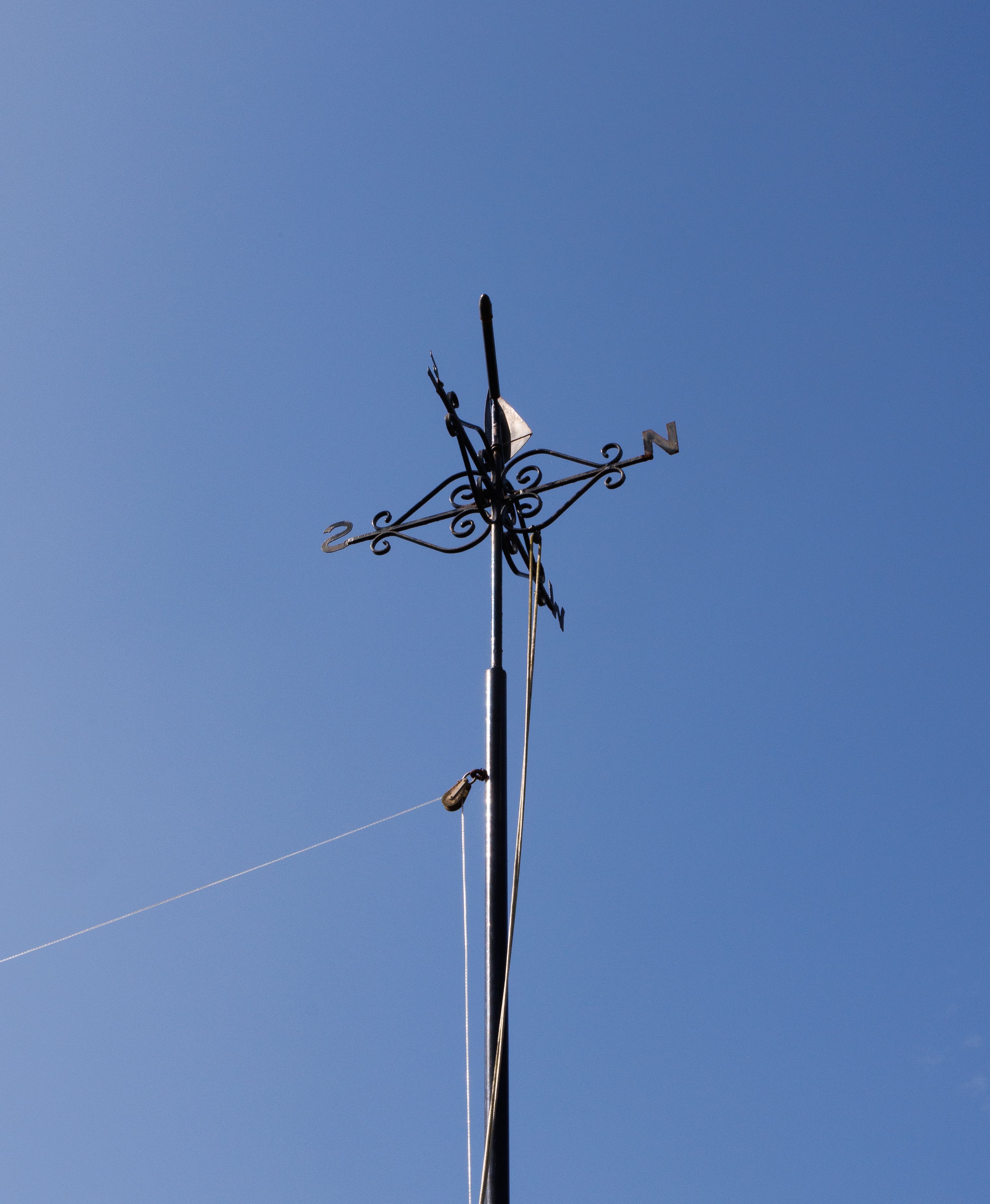 A wind vane on a pole with a blue sky · Free Stock Photo