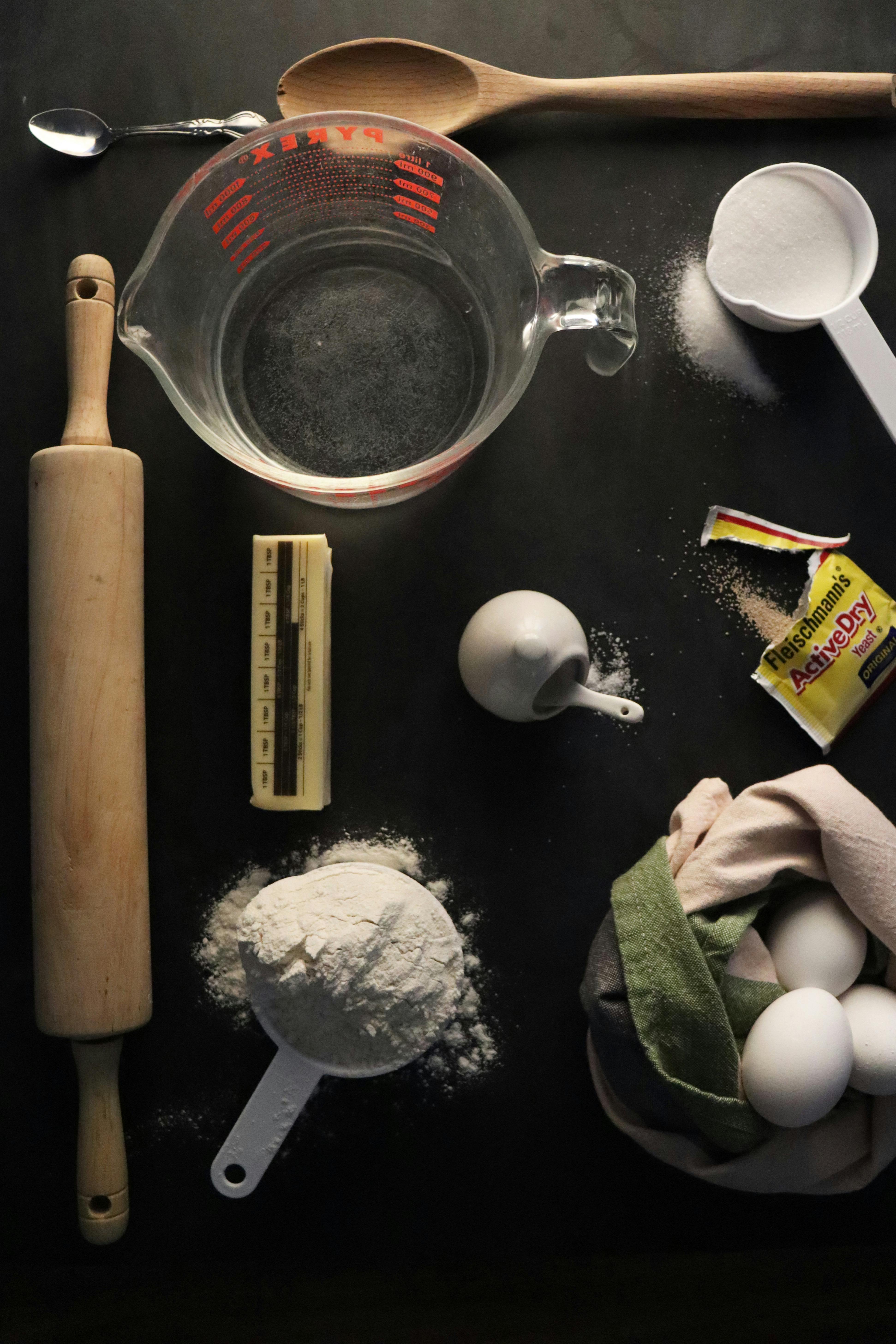 A collection of essential baking ingredients and tools arranged in a dark-themed flat lay.