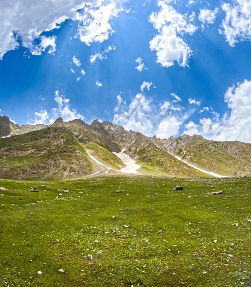 Free A serene meadow with rugged mountains and a bright blue sky, perfect for nature content. Stock Photo