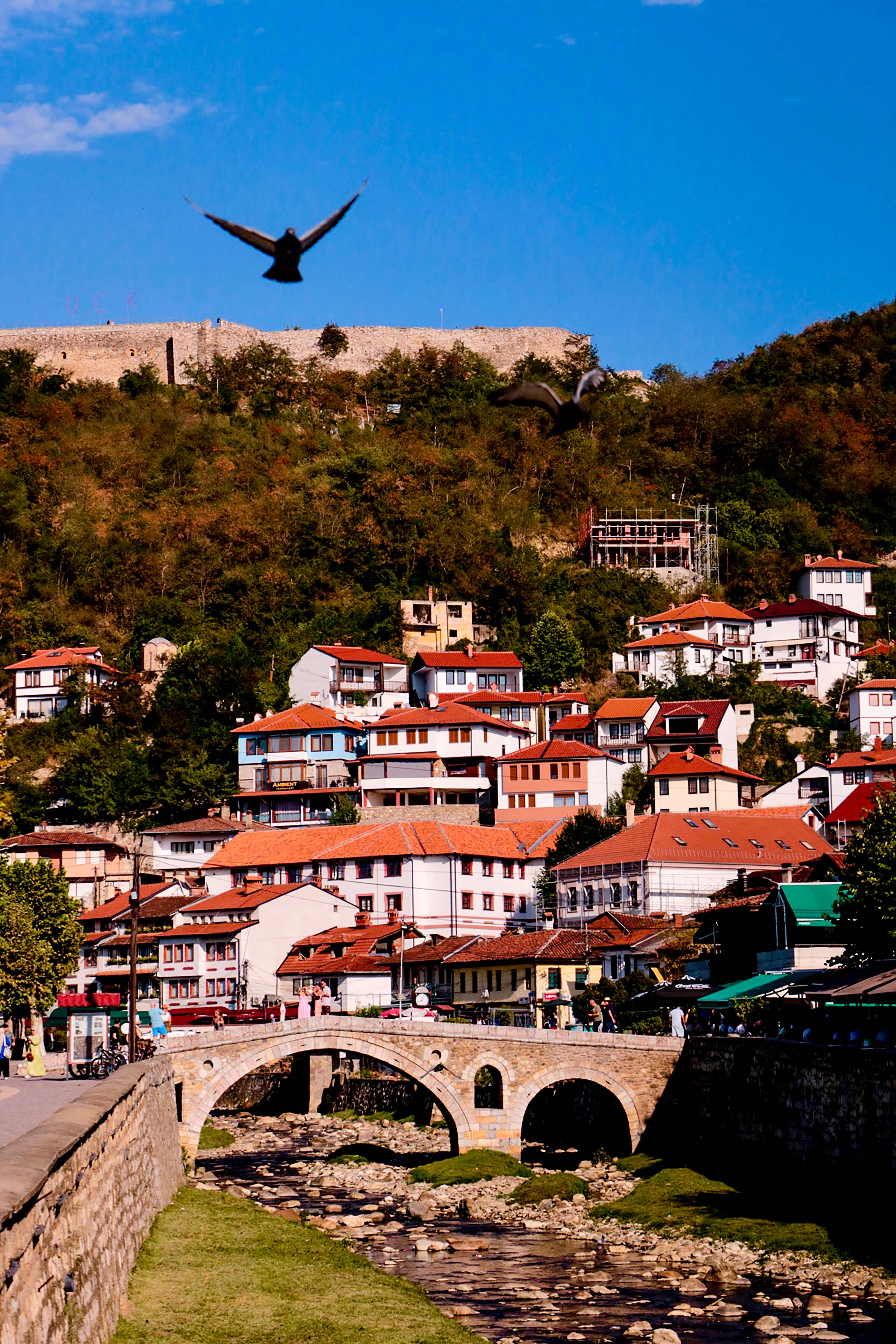 Capture of Prizren with its charming houses and scenic landscape, featuring a historic stone bridge.