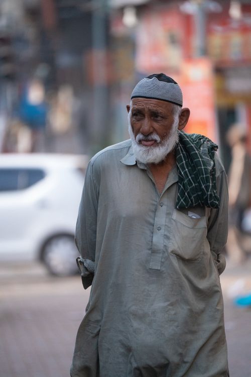 Free A contemplative elderly man walks through a busy street in Karachi, reflecting urban life. Stock Photo