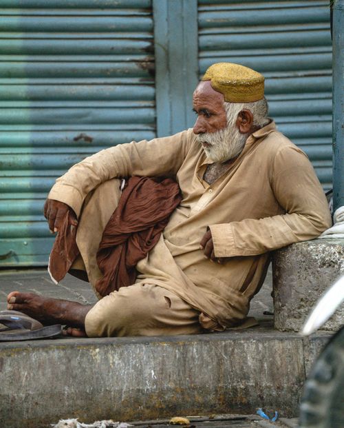 Free A senior man in traditional attire seated on a city street in Karachi, Pakistan, embodying urban lifestyle and resilience. Stock Photo