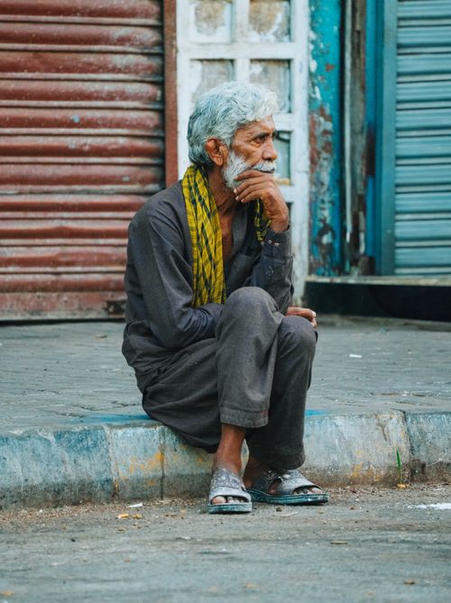 Free Elderly man reflecting on life, seated on Karachi streets, portraying solitude and wisdom. Stock Photo