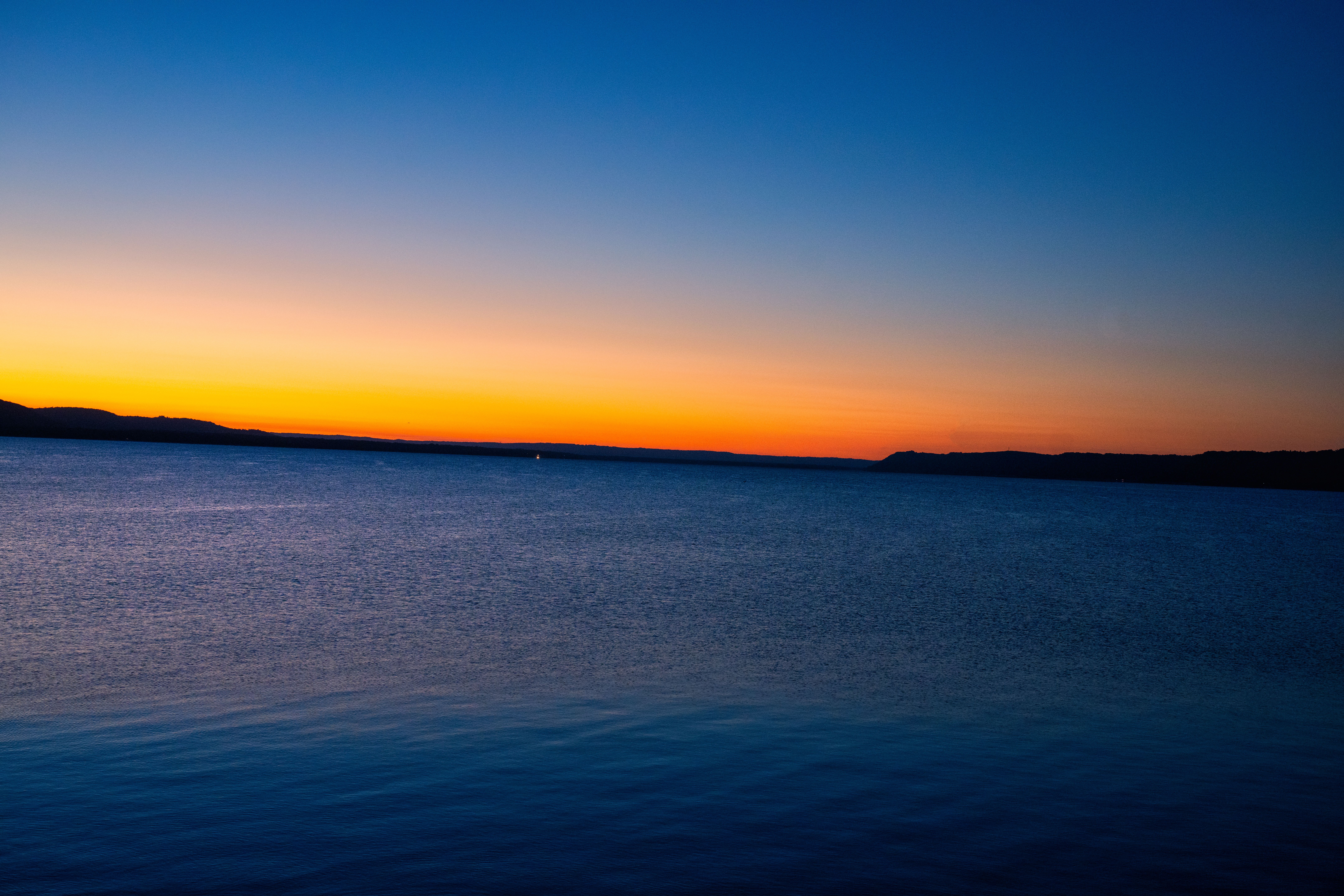 A sunset over a body of water with a blue sky · Free Stock Photo