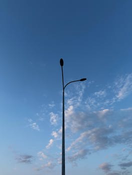 Silhouette of a streetlight with a clear blue sky and clouds.
