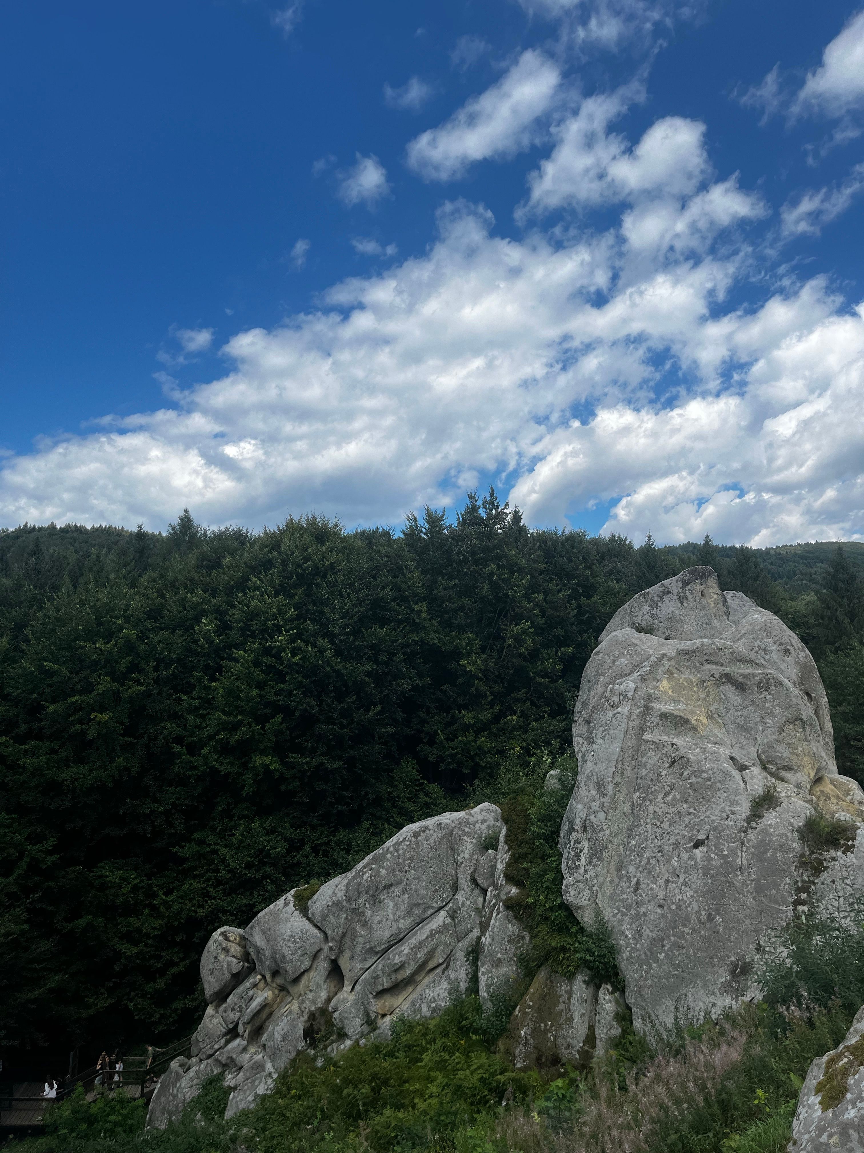 A stunning rock formation set against a forest under a vibrant blue sky.