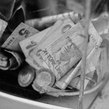 Black and white close-up of Turkish Lira notes and coins in a container.