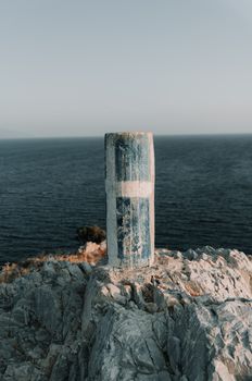 A weathered post stands atop rocky cliffs overlooking the vast ocean at sunset.