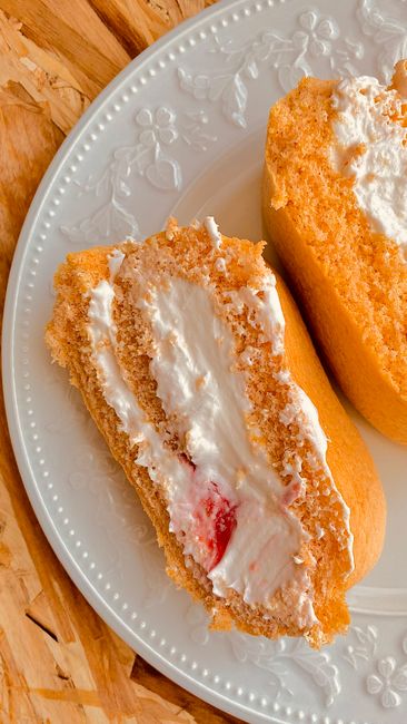 A golden Twinkie sponge cake sliced in half lengthwise, showing the tunnel of white cream filling running through the center.