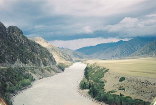 Free A scenic view of a river winding through a mountainous landscape under a cloudy sky. Stock Photo