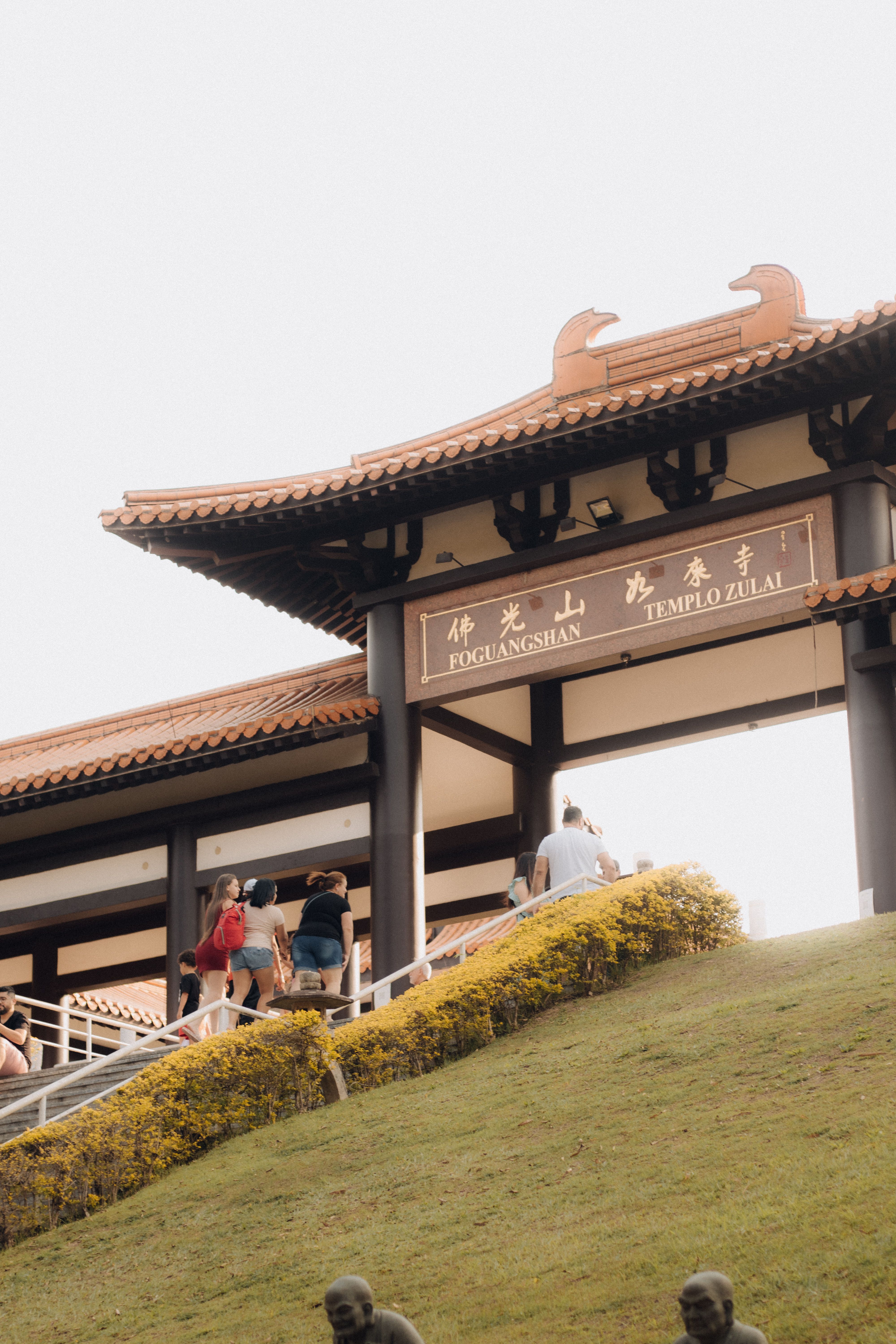 Visitors ascending steps to the Templo Zulai entrance, a Buddhist temple with classic architecture.
