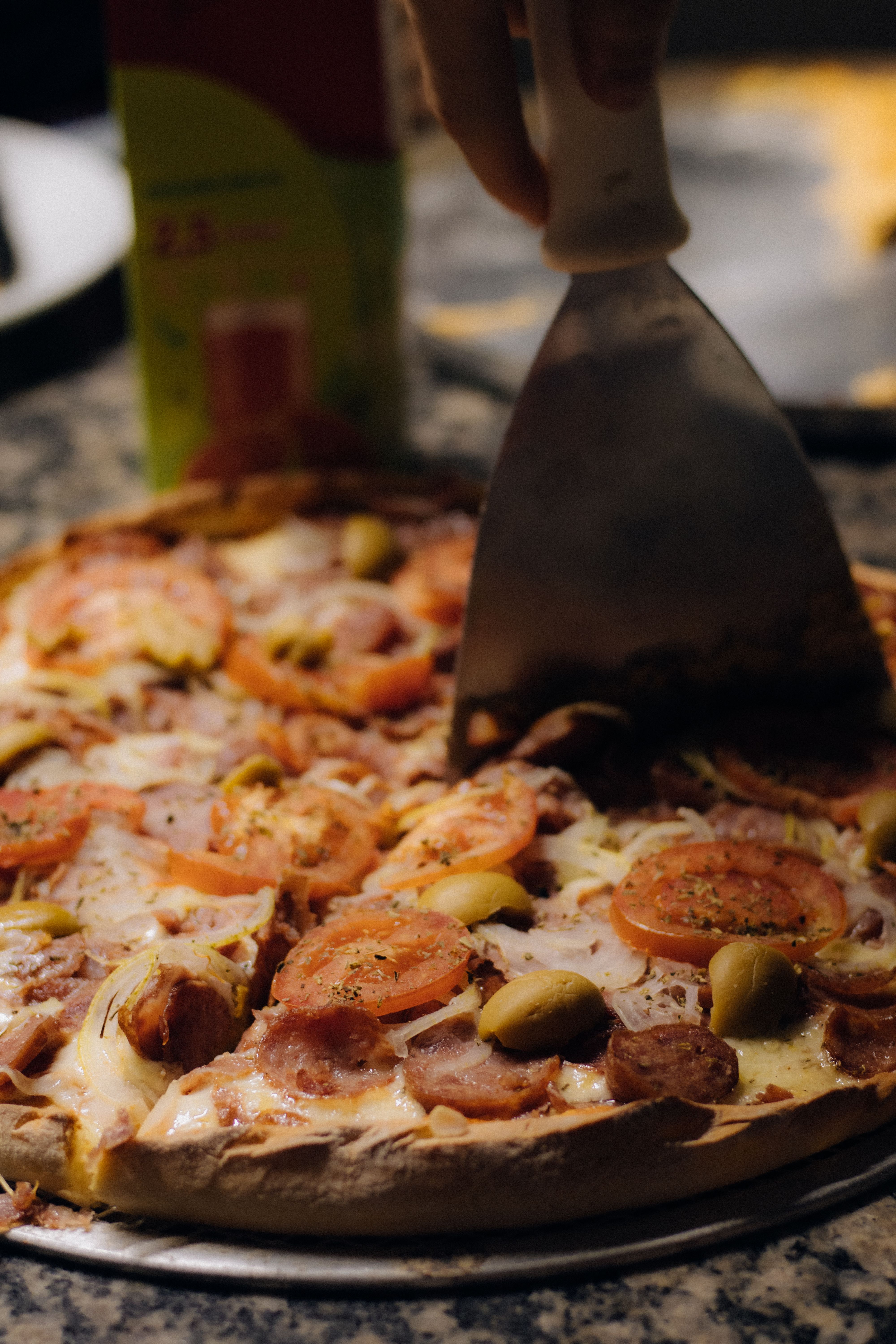 Close-up of a pepperoni pizza being sliced, featuring toppings of olives and cheese.
