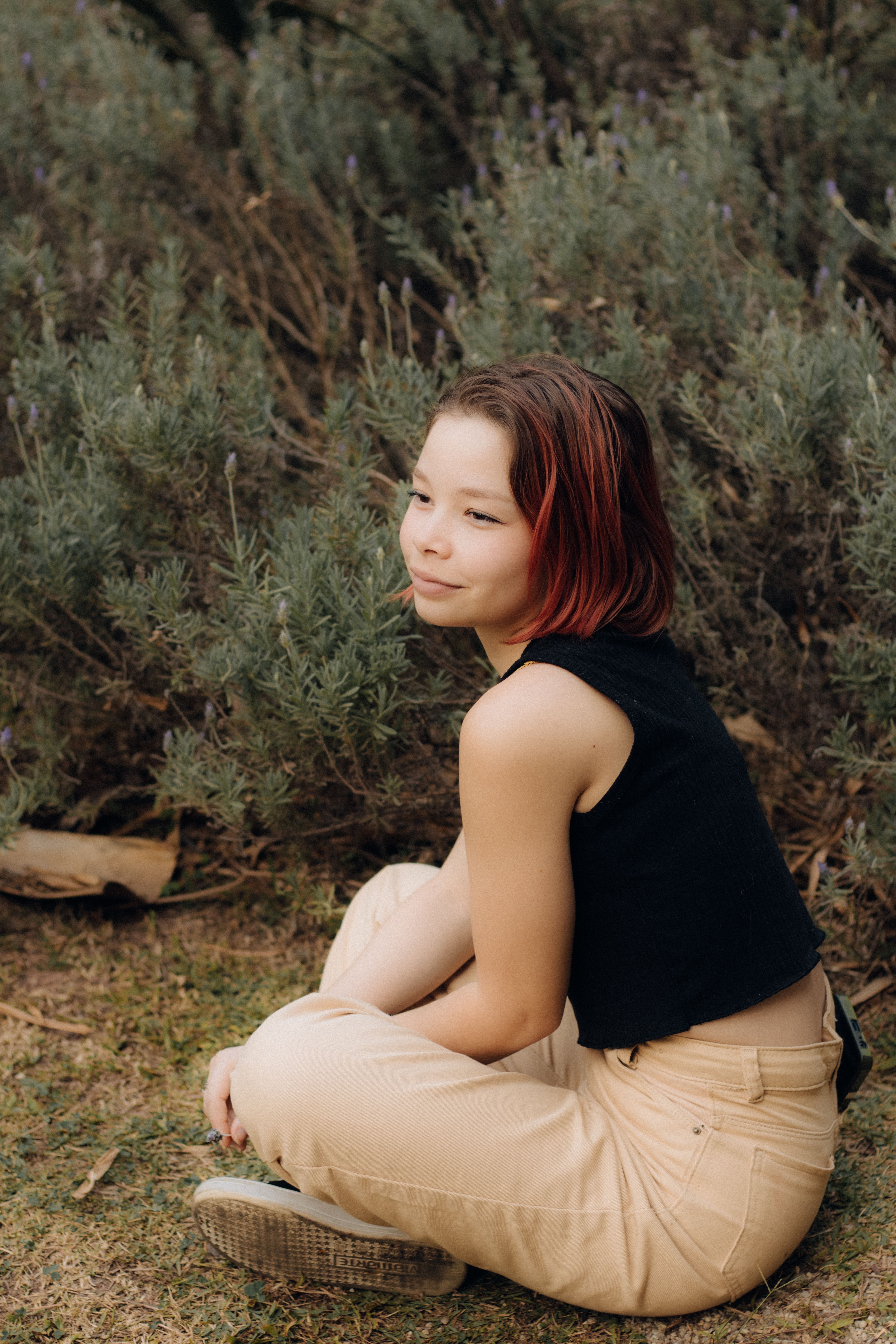 A woman sitting on the ground in front of bushes · Free Stock Photo