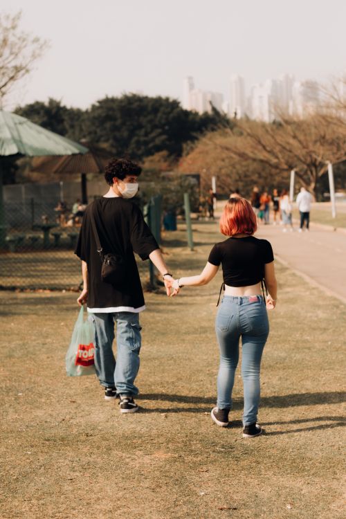 Free A young couple holding hands and walking in a park during the day, showcasing love and leisure. Stock Photo